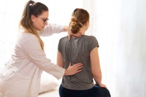 A chiropractor gently adjusts an adult patient's back in a bright, welcoming treatment room.