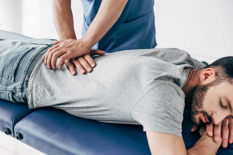 A therapist guides a patient through a strengthening exercise beside a treatment table.
